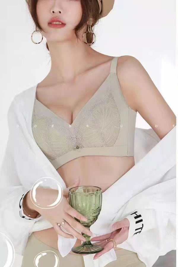 A woman wearing a beige embroidered wireless contour bra with a white open-front cardigan, holding a green glass on a clean white background.